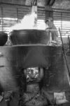 an enormous cauldron on a wood fire and a man stirring a soup